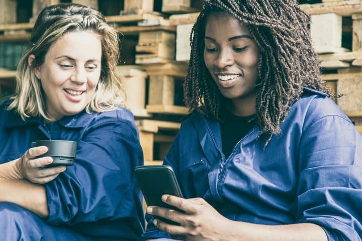 Two factory colleagues in overalls watch content on mobile phone
