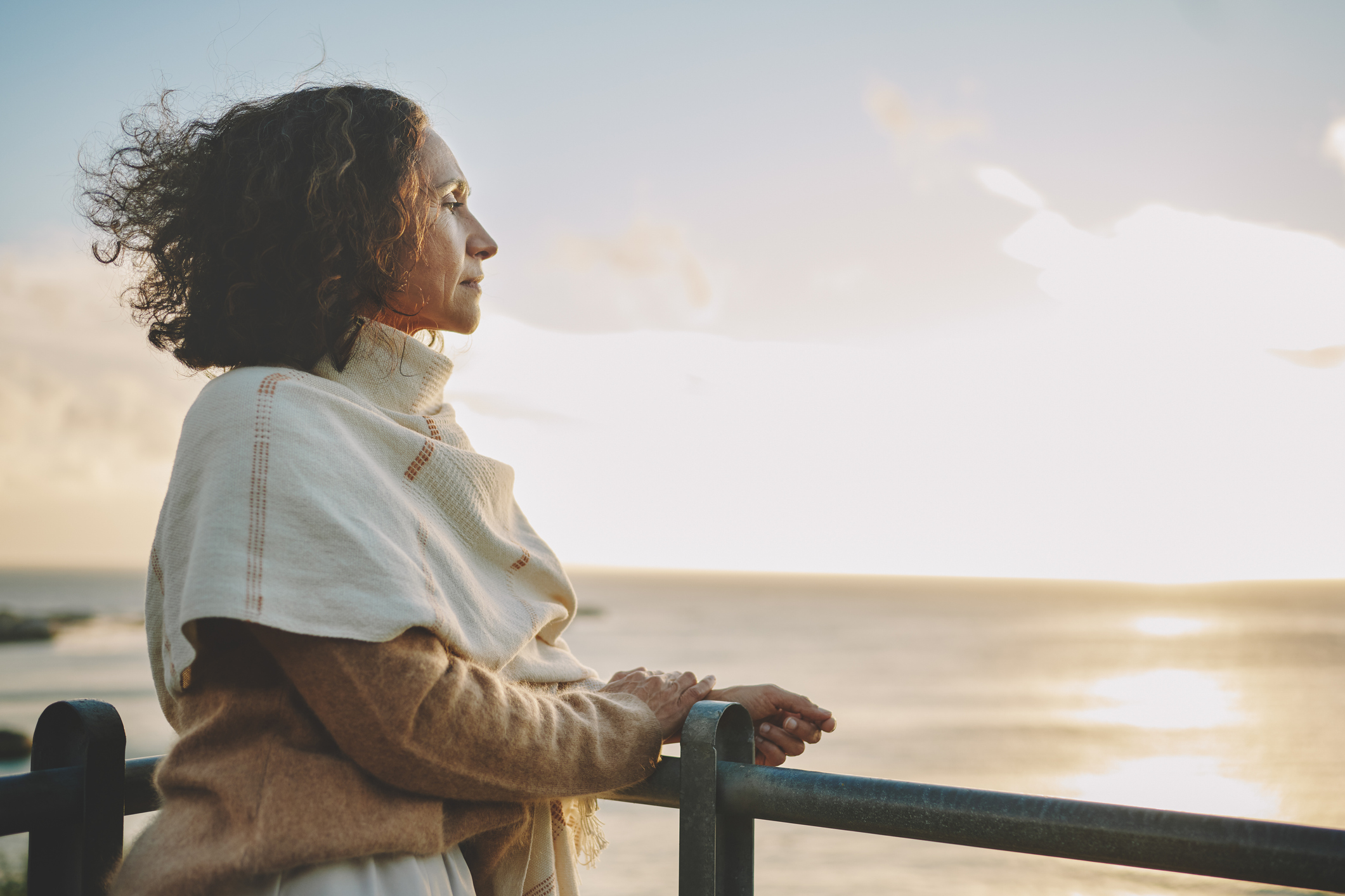 Mature woman leaning on a railing and looking out at the sunset over the ocean
