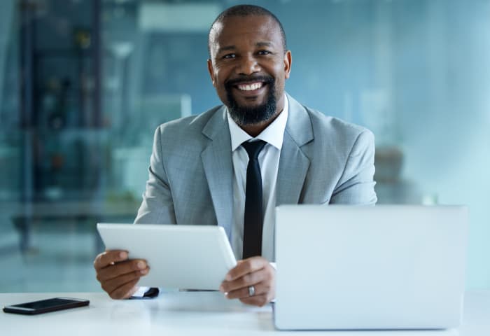 Smiling businessman working on a digital tablet and laptop in an office