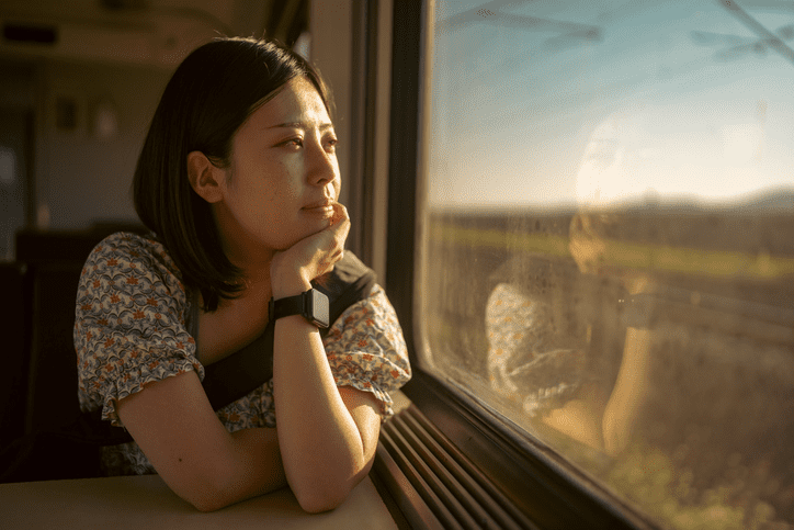 Portrait of young female tourist traveling by train. She is sitting at the seat next to the window and looking outside at the view through the window.