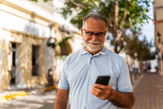 Senior man walking and using mobile phone outdoors