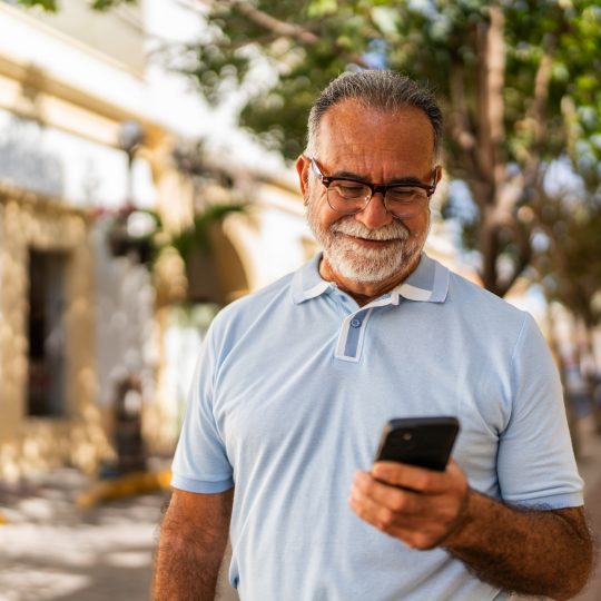 Senior man smiling looking down at a mobile phone in his left hand
