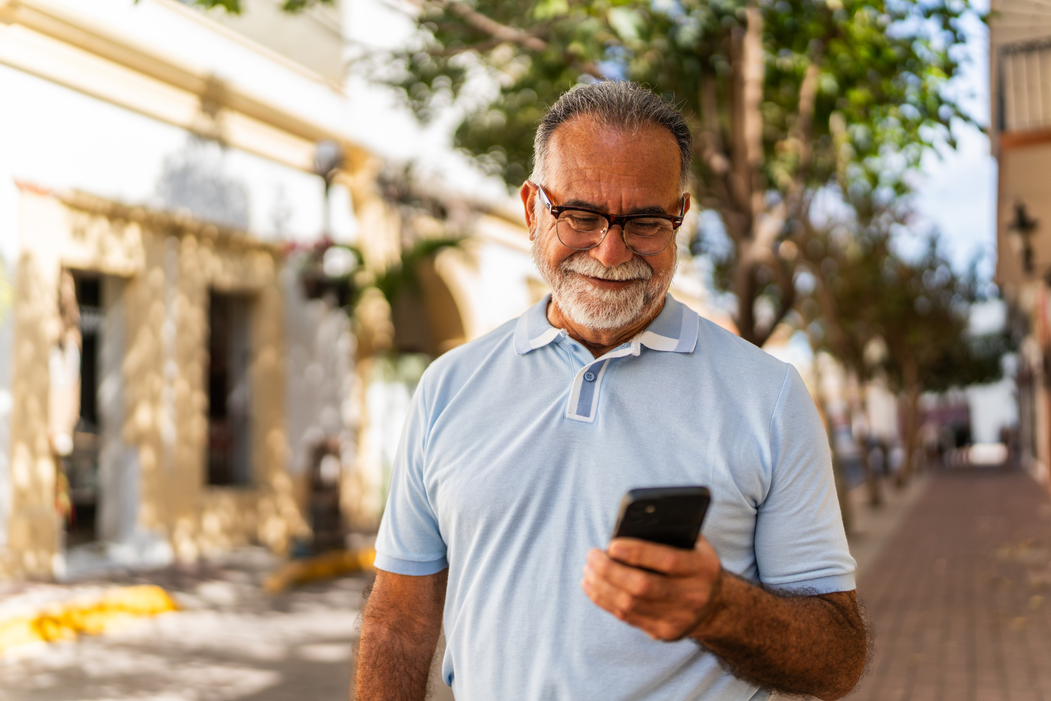 Senior man smiling looking down at a mobile phone in his left hand