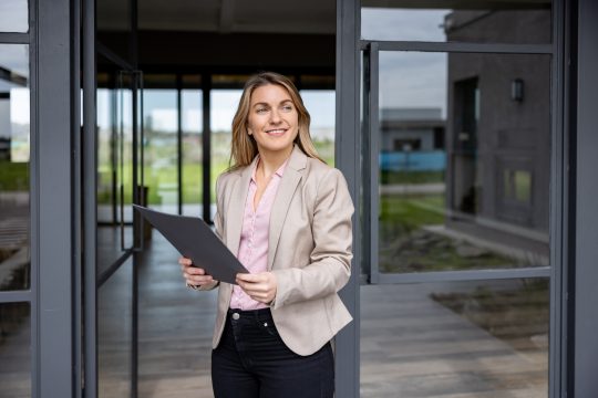 Portrait of a woman showing a house for sale and looking at the camera smiling