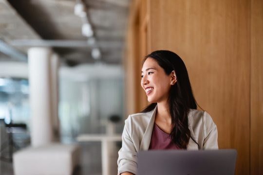 Young Asian woman smiling looking off camera with a laptop in front of her