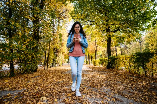 Caucasian woman using her smart phone while walking in a park