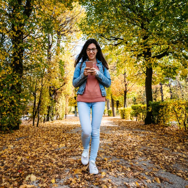 Young white woman walking through a park looking down at her phone