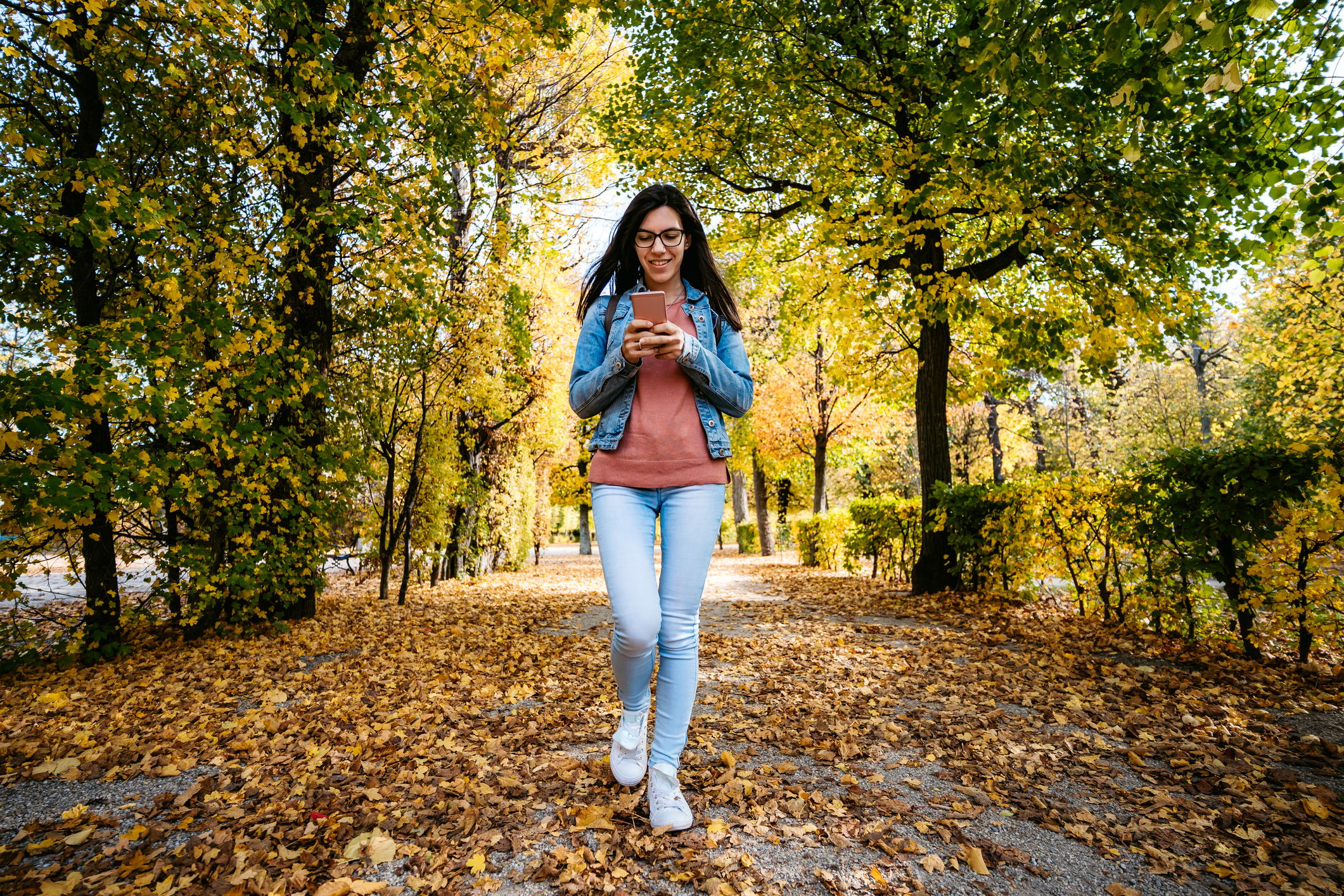 Young white woman walking through a park looking down at her phone