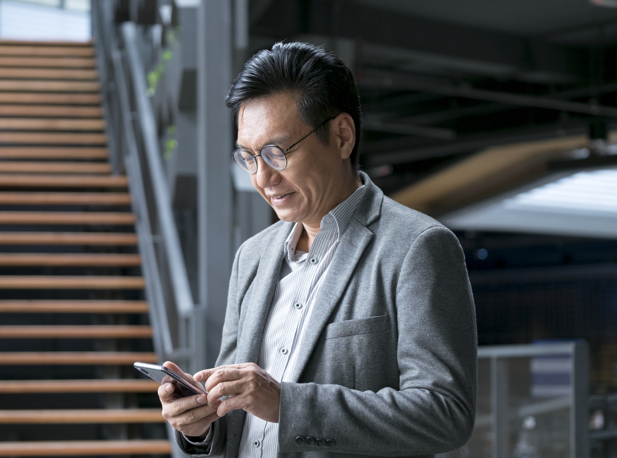 A mature Asian man dressed in business attire looking down at a mobile phone in his hand