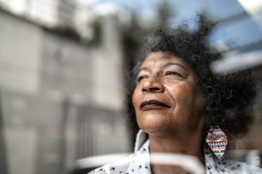 Senior woman looking through the window at home smiling