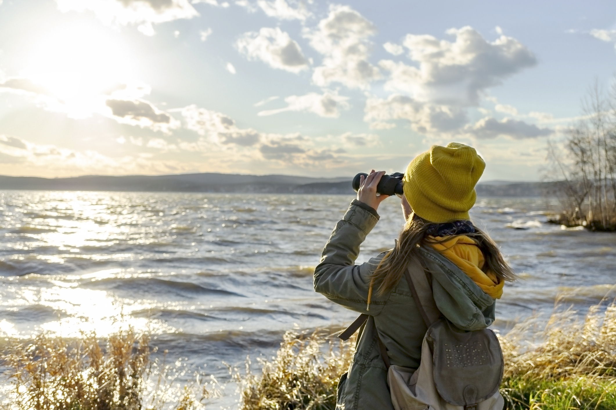Young woman watching birds with binocular on lake.