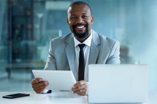 Portrait of a mature businessman working on a digital tablet and laptop in an office