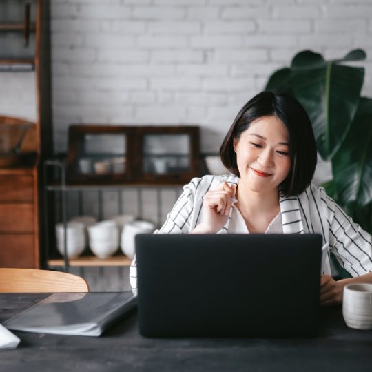 Young Asian woman having online business meeting, video conferencing on laptop with her business partners, working from home in the living room