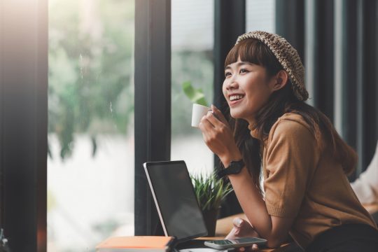 Young Asian woman playing on the phone and drink coffee at a coffee shop.