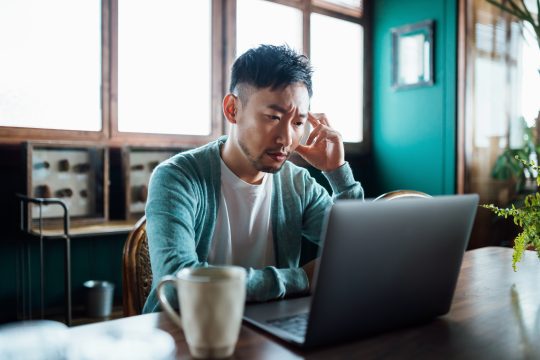 man looking worried with hand on head while using laptop