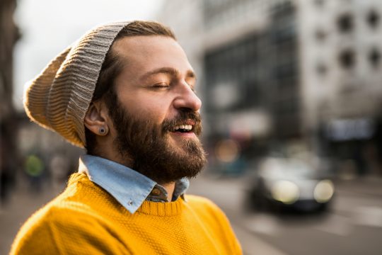 A young hipster looking white man with his eyes closed taking a deep breath inward