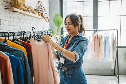woman picking up pink top from clothing rack
