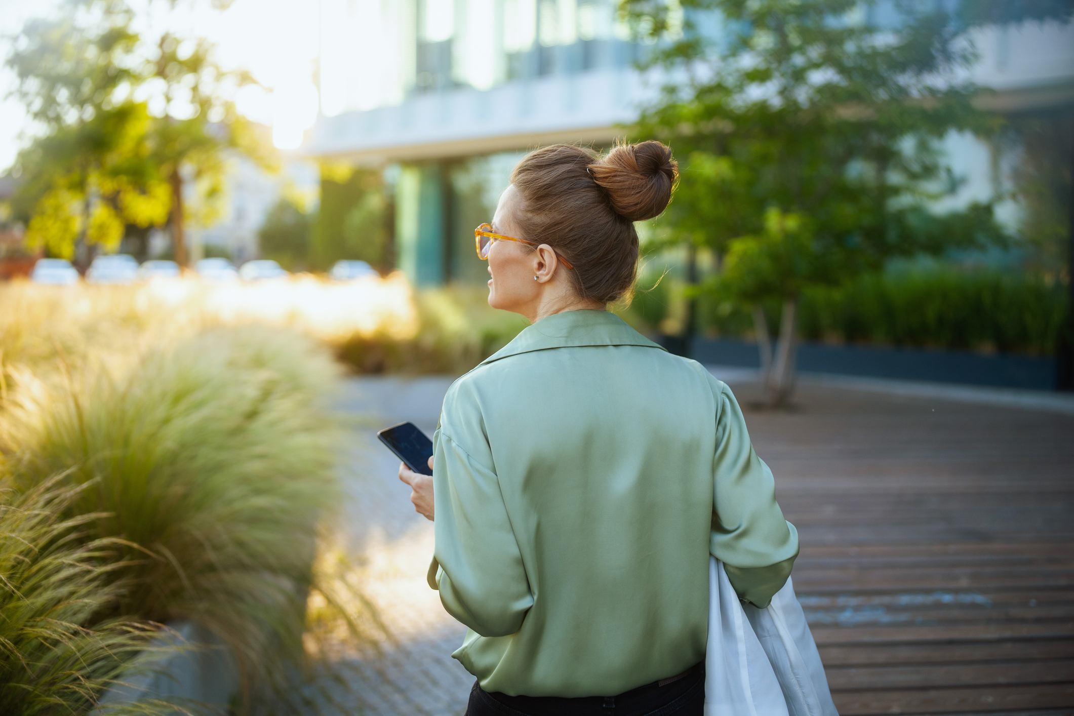 Middle aged white woman faced with her back toward the camera while she walks away holding a mobile phone