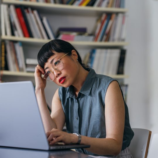 Middle aged Asian woman looking stressed looking at laptop