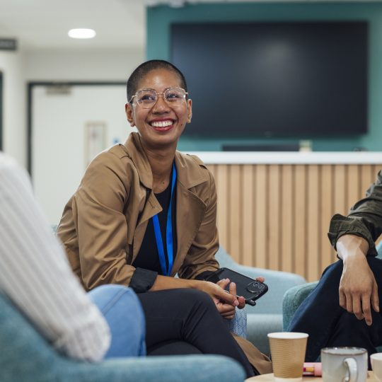 A group of healthcare professionals sitting in chairs around a wooden table in a staff common room