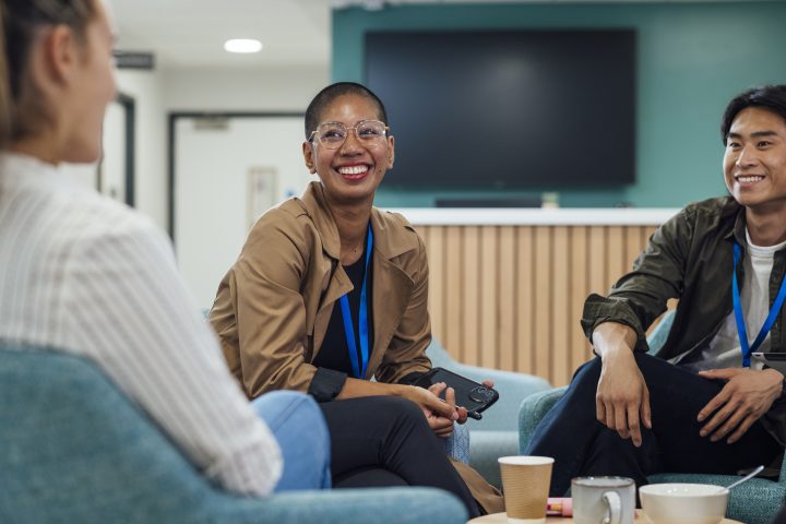 A group of healthcare professionals sitting in chairs around a wooden table in a staff common room