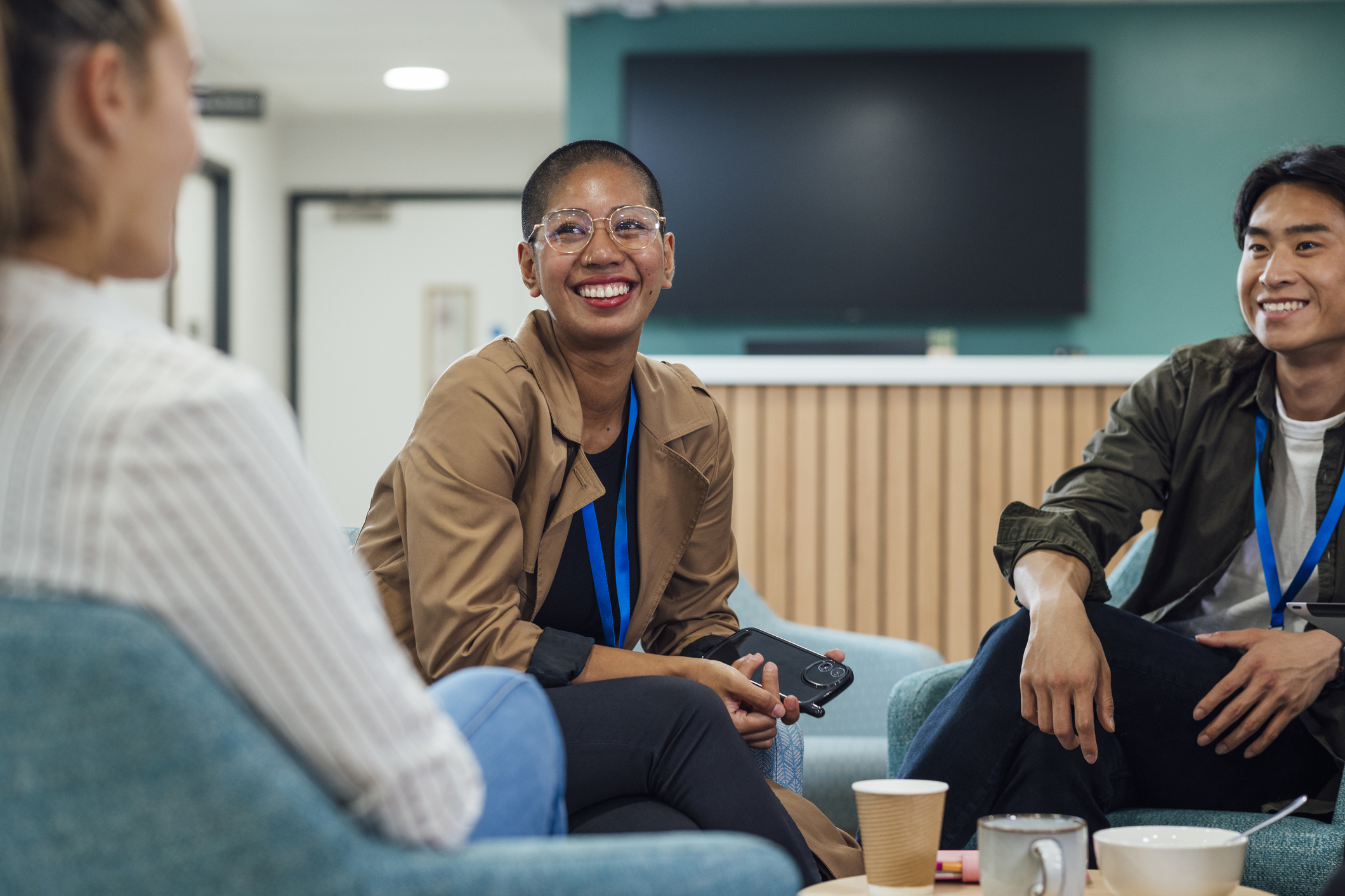 A group of healthcare professionals sitting in chairs around a wooden table in a staff common room