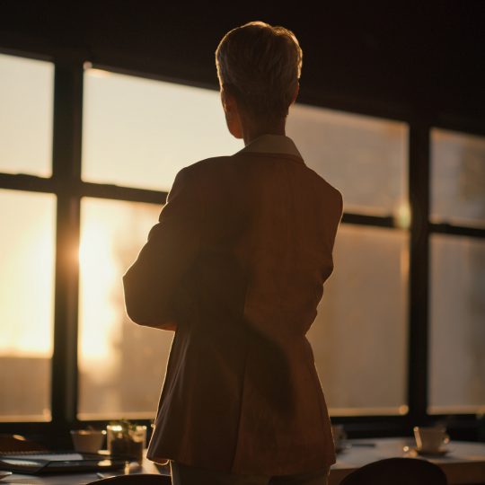 Sunset, window and back of woman in the office thinking, planning and brainstorming for project.