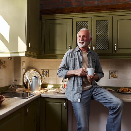 Happy mature man day dreaming during coffee time at home.
