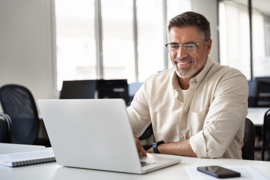 Happy smiling mature business man using computer, typing and working in modern office