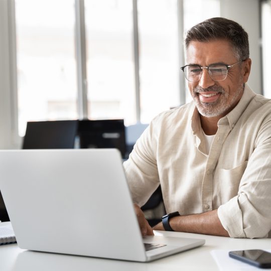 Happy smiling mature business man using computer, typing and working in modern office