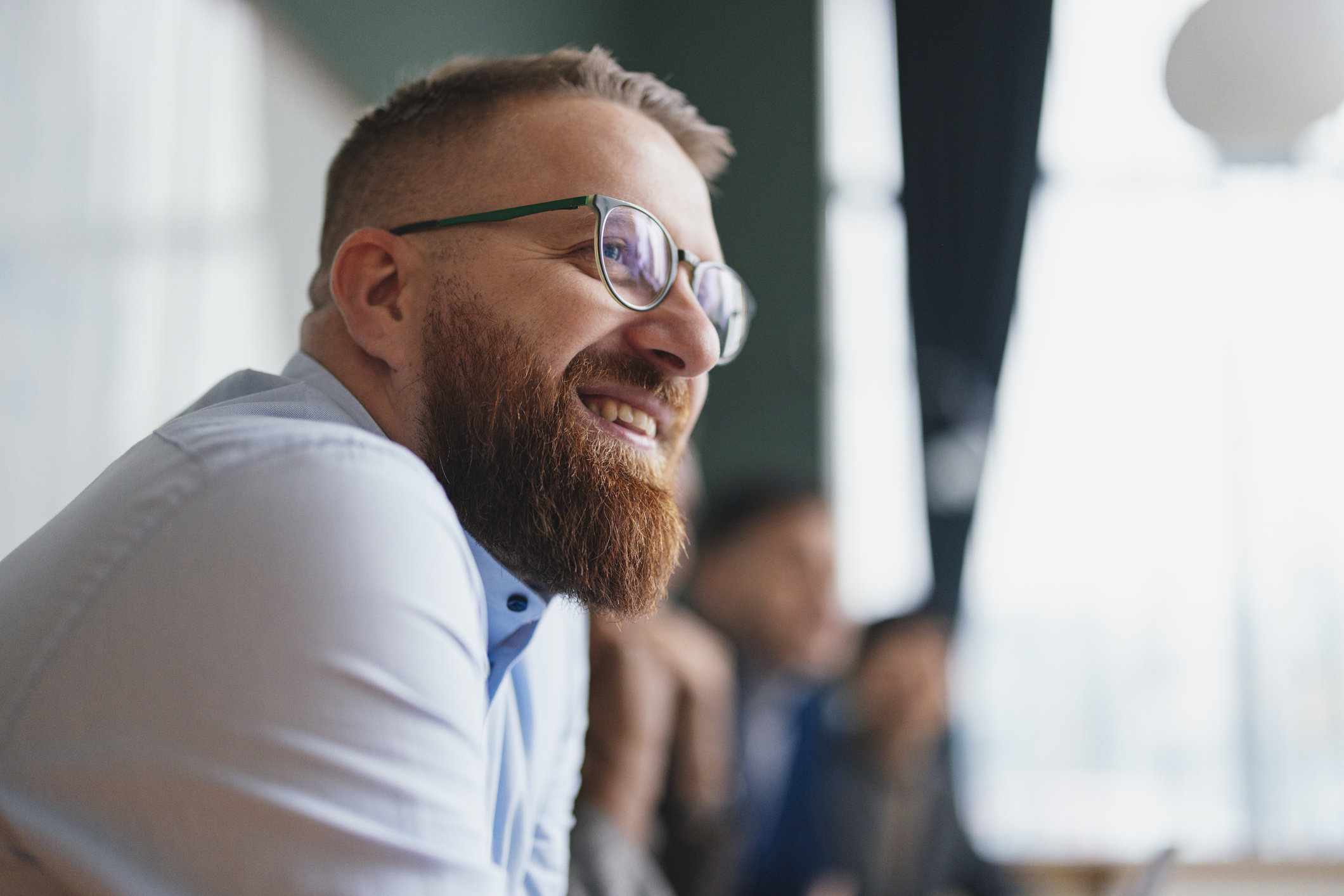 A close up of a young white man wearing glasses who is smiling looking to the right of the camera