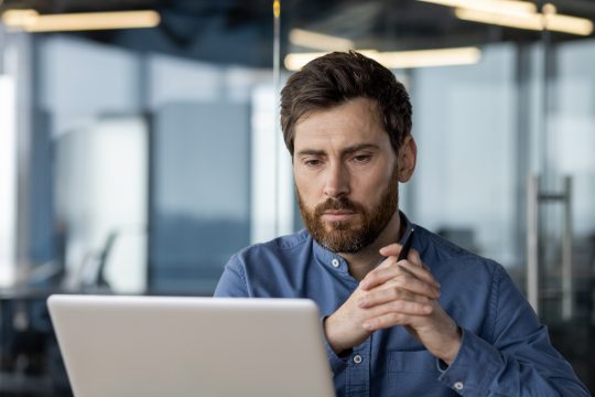 Close-up photo of a thoughtful and serious young man sitting at a desk in the office