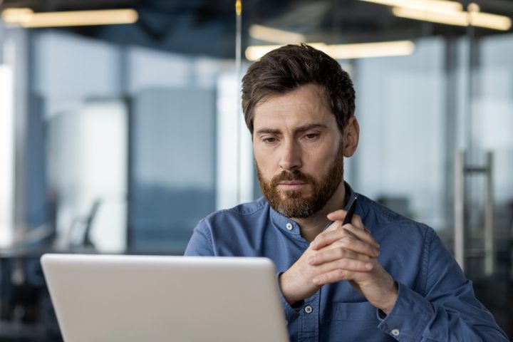 Close-up photo of a thoughtful and serious young man sitting at a desk in the office
