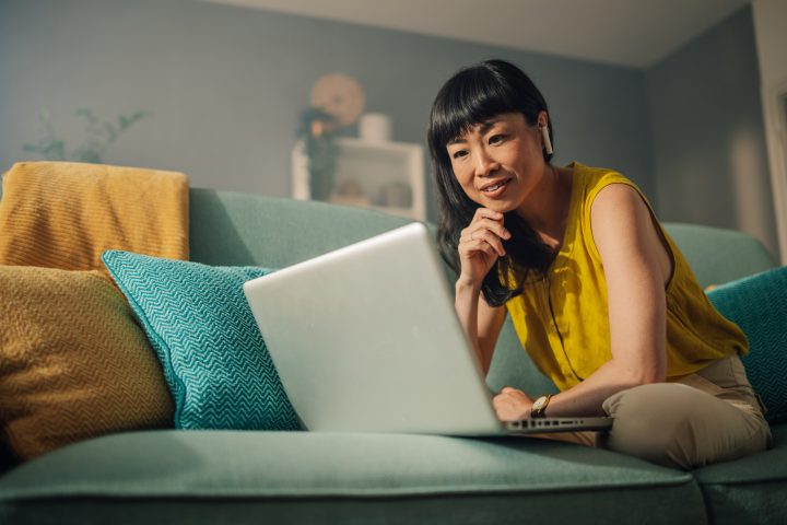 Focused woman with laptop on green couch, hand on chin thoughtfully.