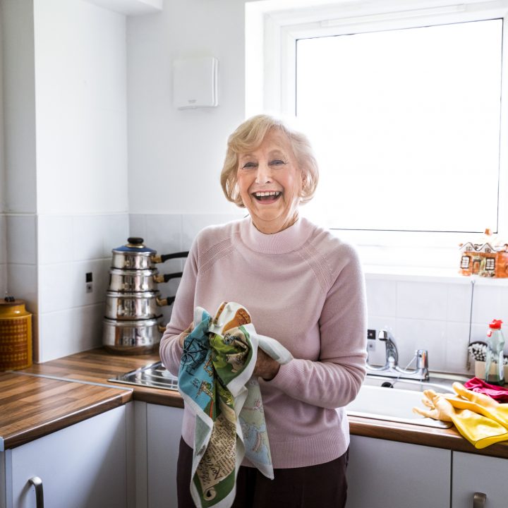 Elderly woman stood smiling while holding a kitchen towel