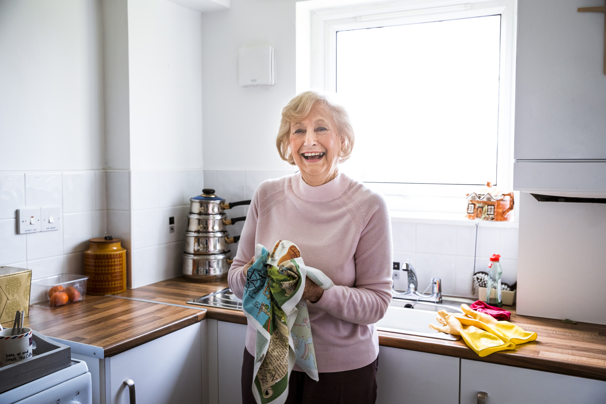 Elderly woman stood smiling while holding a kitchen towel