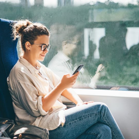Young woman traveling by train and using phone