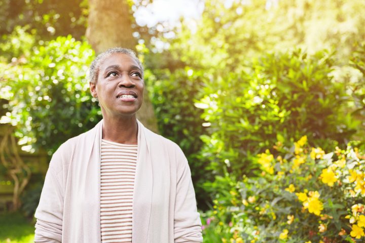 A confident mature woman happily standing outside in a garden and thinking