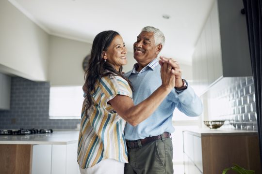 A happy elderly couple is dancing in the kitchen