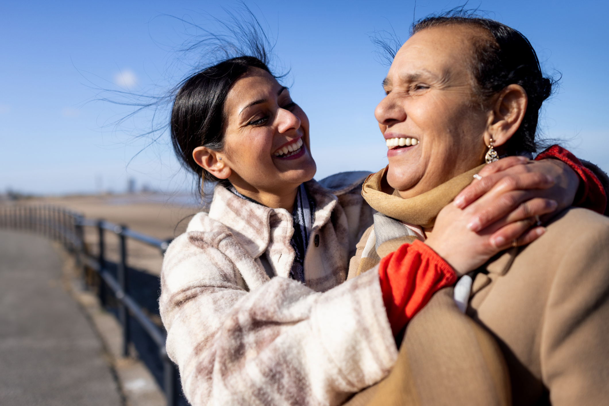 Waist-up shot of a granddaughter and grandmother walking with each other along a promenade next to a beach