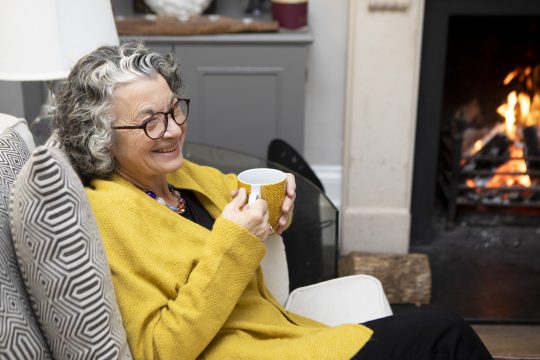 mature adult sitting by a fireplace in a living room at home