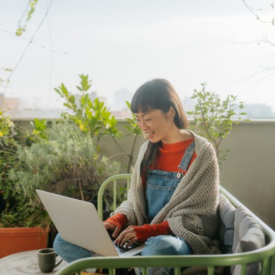 Photo of a smiling Japanese woman having a video call while sitting on the balcony of her loft apartment