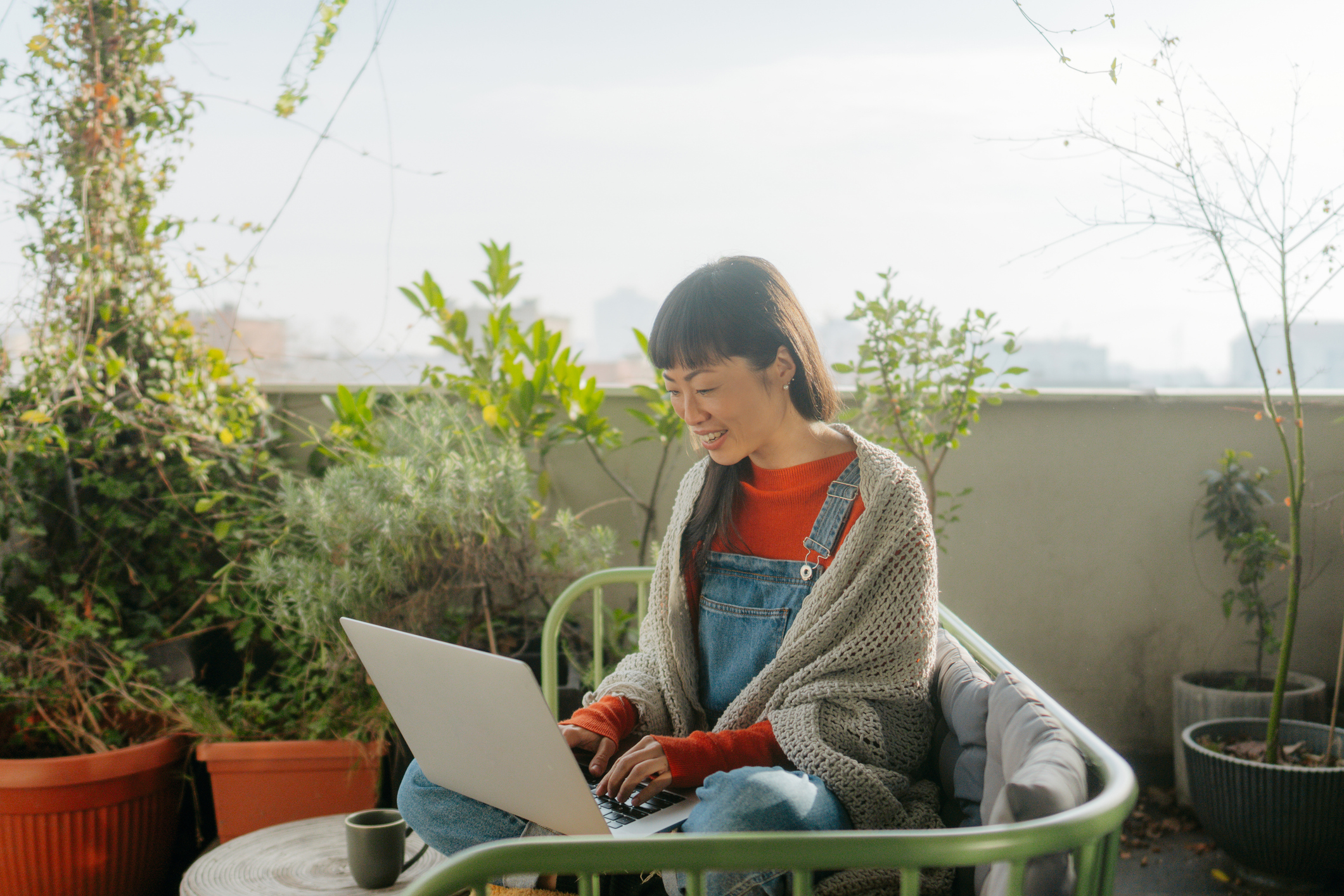 Photo of a smiling Japanese woman having a video call while sitting on the balcony of her loft apartment
