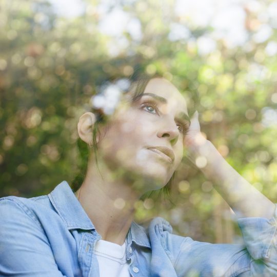 Young white woman looking stressed. The reflection of a window overlays her in the image