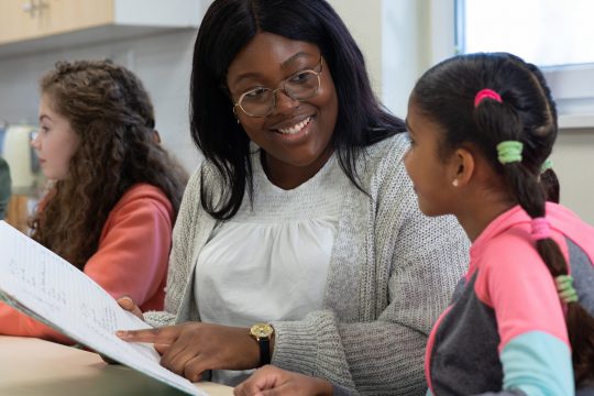 A small group of children sit around a table with a young female therapist in a community centre