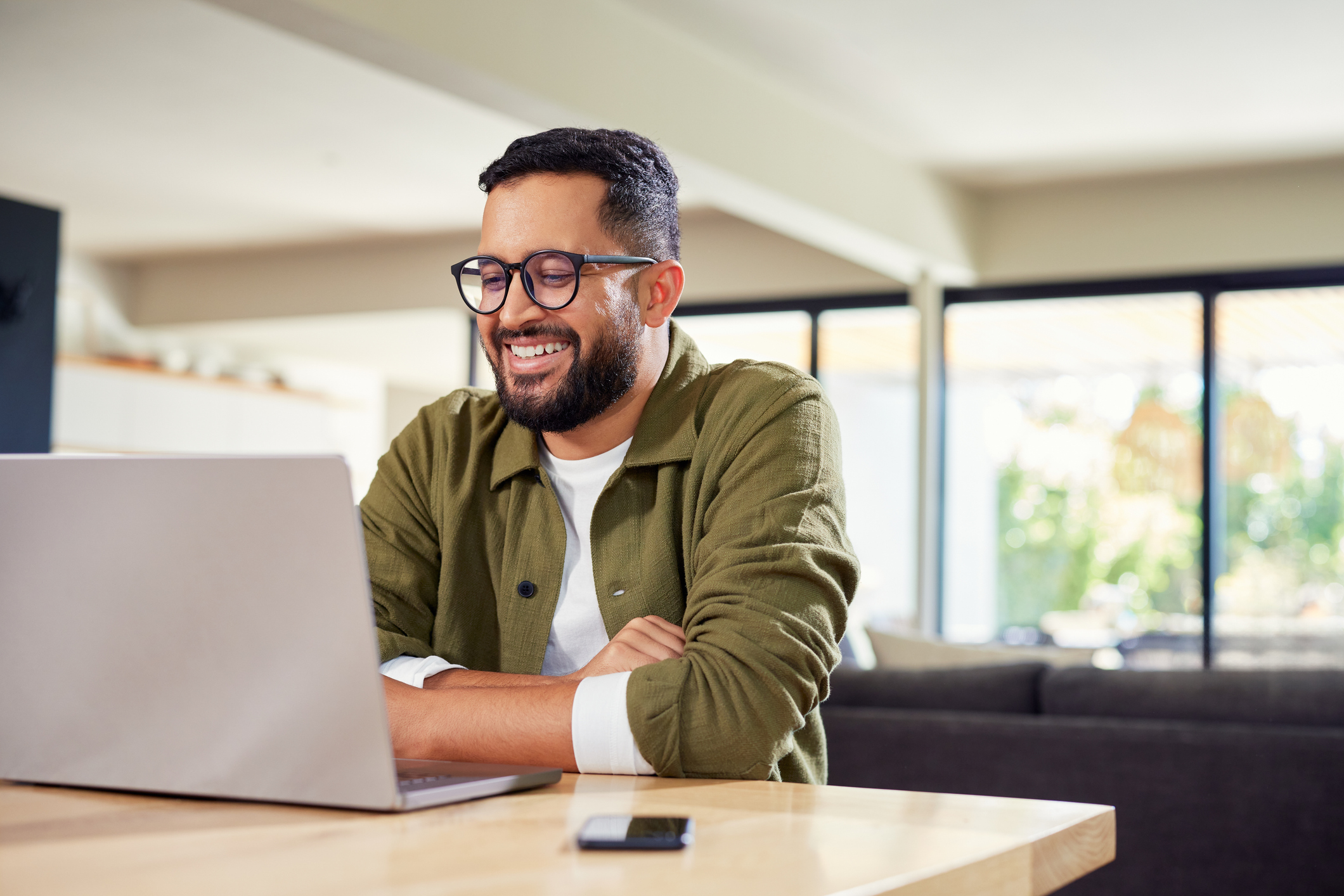 Smiling young Indian man sitting at home while using laptop