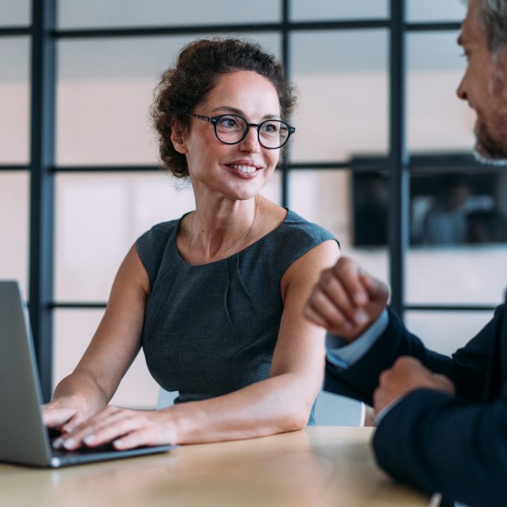 Shot of a two confident business persons sitting on a desk in the office and sharing ideas
