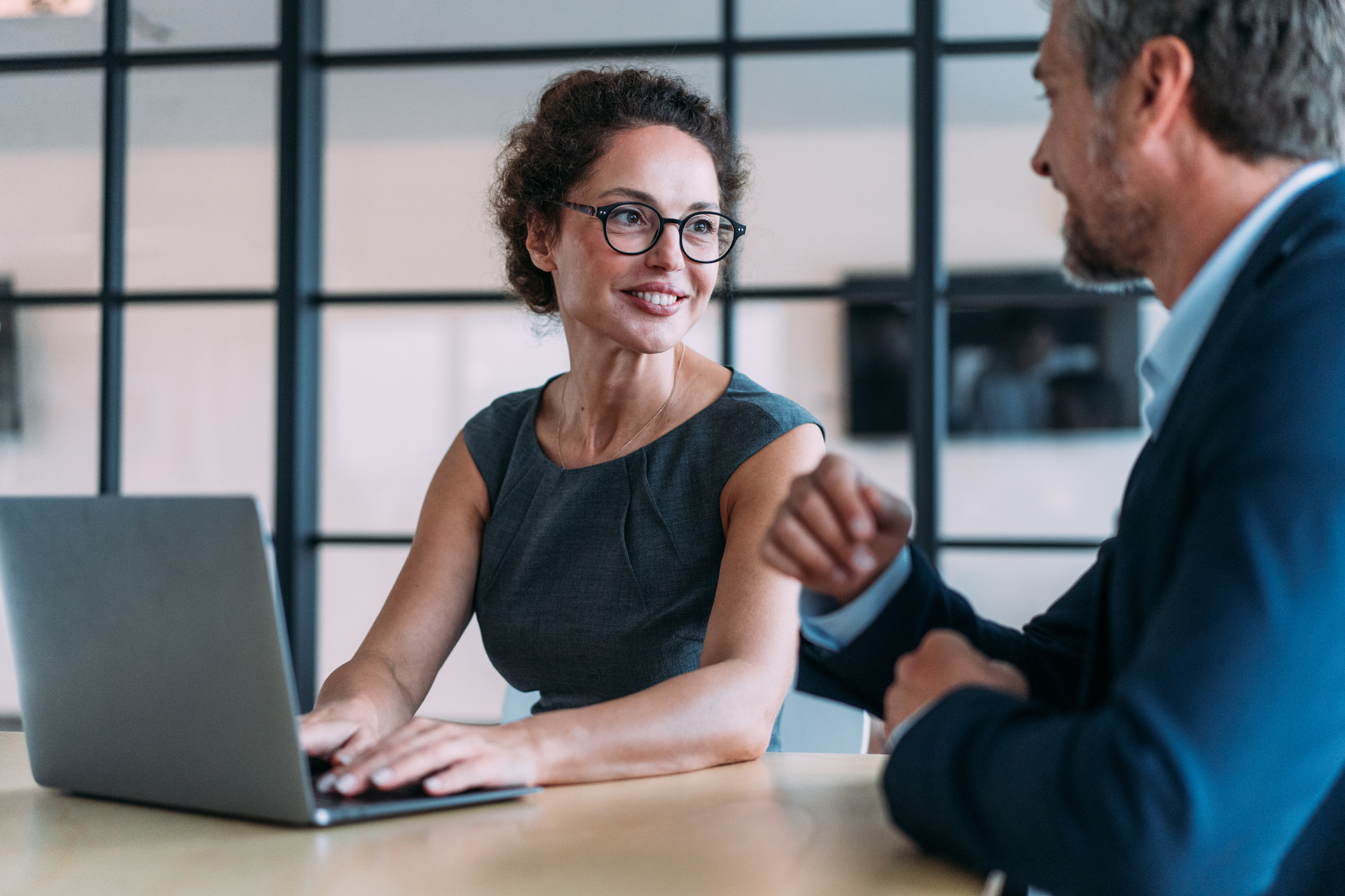 Shot of a two confident business persons sitting on a desk in the office and sharing ideas