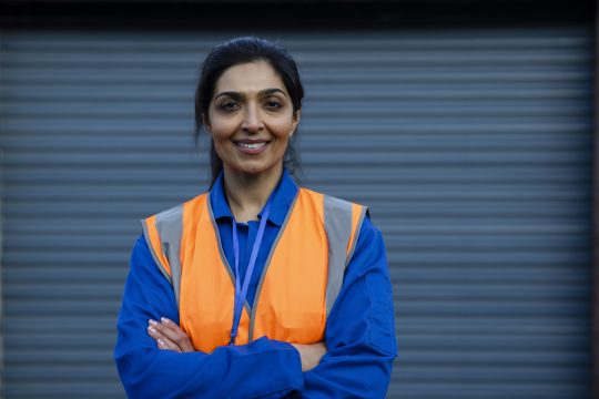 Female worker smiling, wearing coveralls looking at the camera.