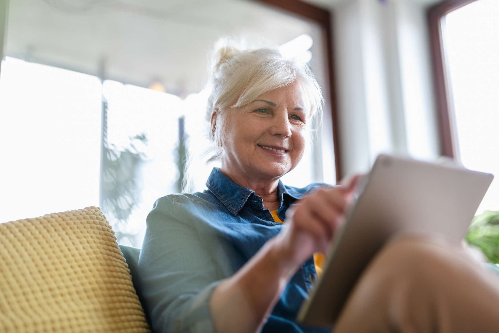 Mature woman using digital tablet while sitting on sofa at home